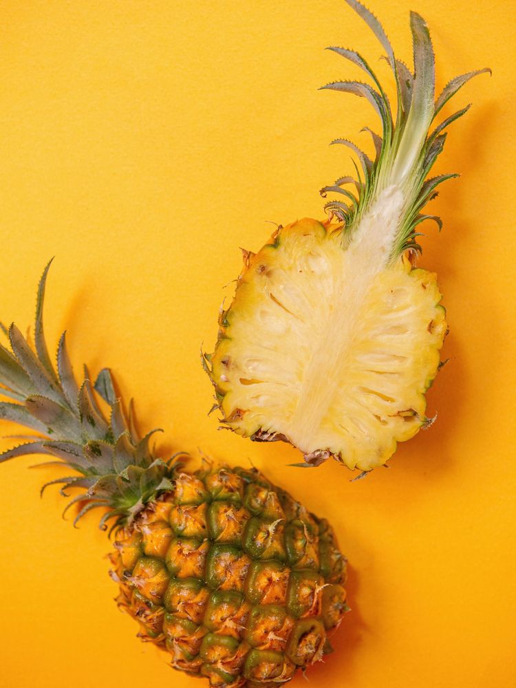 A halved pineapple showing its core beside a whole pineapple