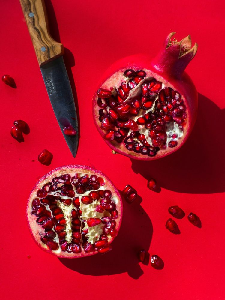 Two pomegranate halves cut open with loose seeds and a knife