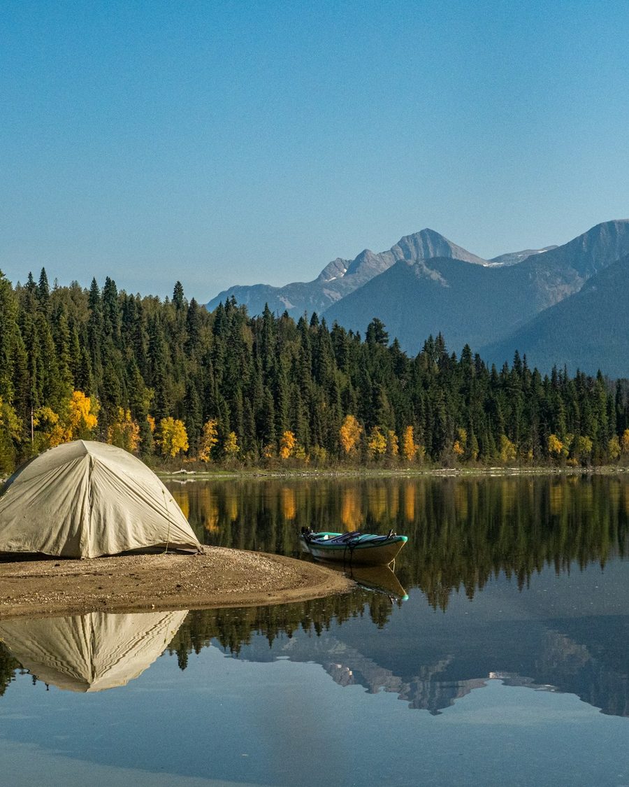 A tent and boat on a calm lake shore among mountains